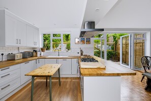 A modern kitchen with white cabinetry, a wooden countertop, a central island, and a view of greenery outside. - Stylish Spacious Brighton Home | Parking & Garden - Pass the Keys (Brighton)