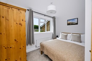 Een slaapkamer met een bed, een raam, een radiator en een houten garderobe.