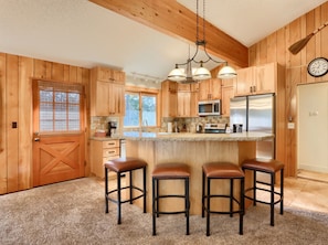A kitchen with wooden cabinets, a central island with stools, a microwave, and a refrigerator. - Cabin (10B) Arrow Lodge (Yosemite National Park)