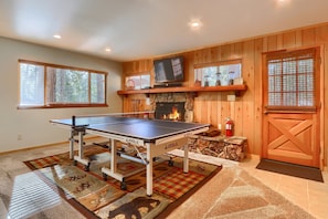 A ping pong table in a room with wooden walls, a fireplace, and a door with a window. - Cabin (10B) Arrow Lodge (Yosemite National Park)