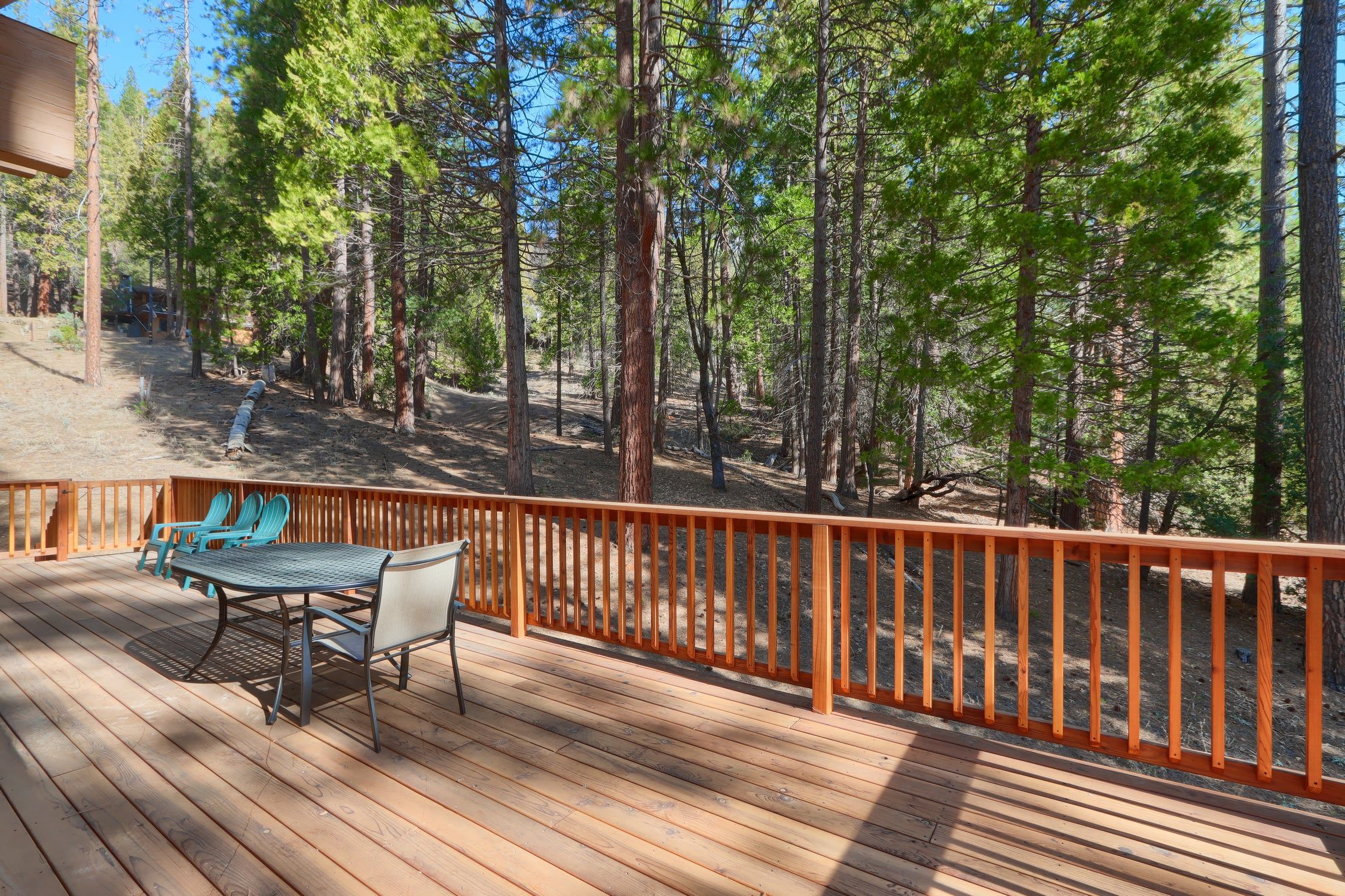 A wooden deck with outdoor furniture, surrounded by a wooden railing, overlooking a forested area.