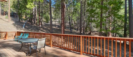 A wooden deck with outdoor furniture, surrounded by a wooden railing, overlooking a forested area.