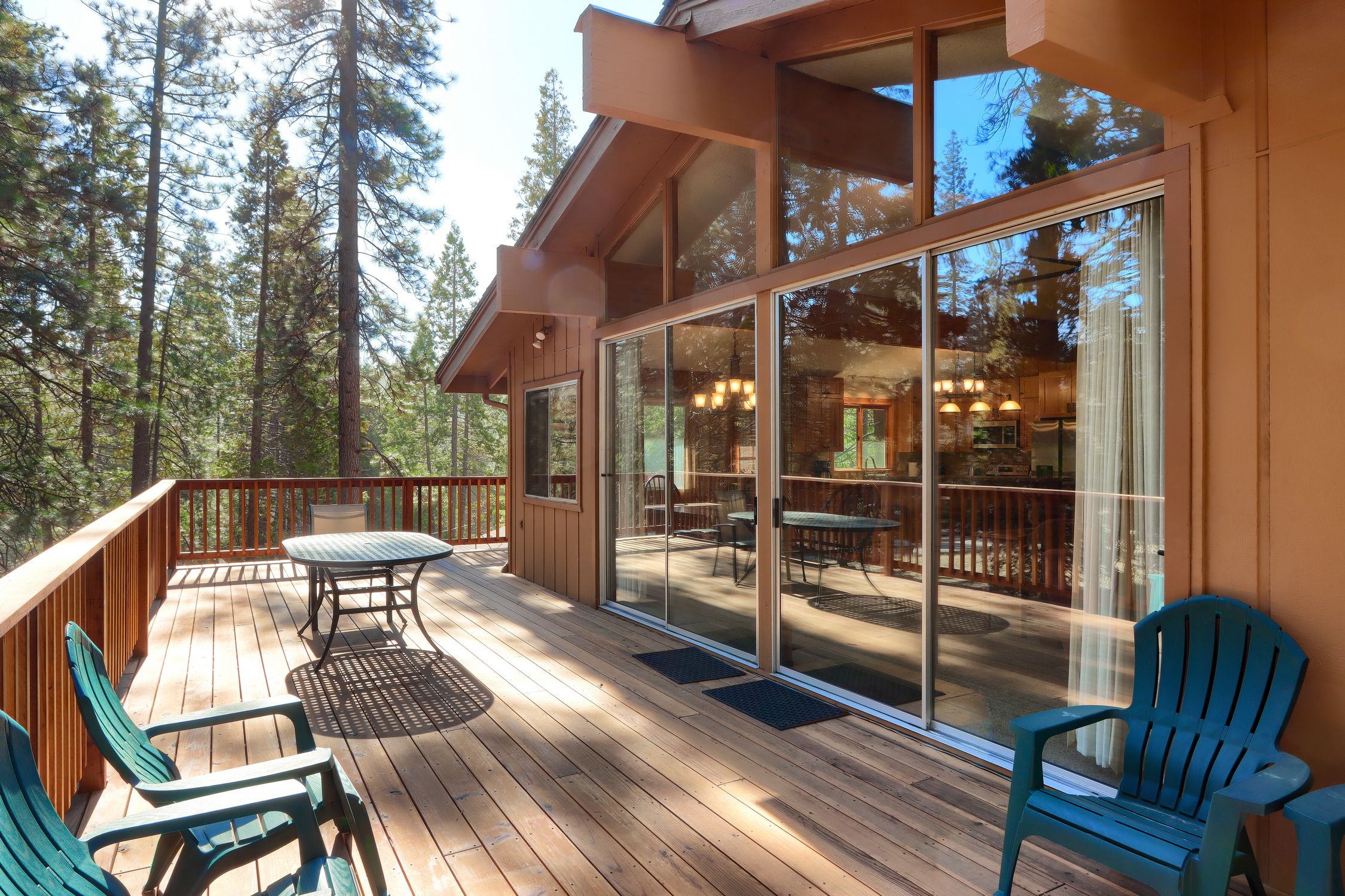 A wooden deck with outdoor furniture, large sliding glass doors, and a view of a forested area.