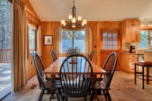 A wooden interior with a dining table, chairs, a chandelier, and a kitchen area. - Cabin (10B) Arrow Lodge (Yosemite National Park)