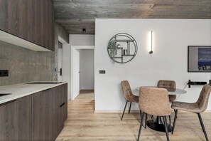 A modern kitchen with wooden cabinets and a dining area with a round table and chairs. - Luxury Apt. Downtown Reykjavik - Best Location (Reykjavík)
