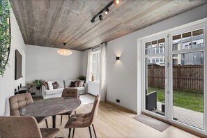 A modern interior with a dining area, a sofa set, and a large sliding glass door leading to a backyard. - Luxury Apt. Downtown Reykjavik - Best Location (Reykjavík)