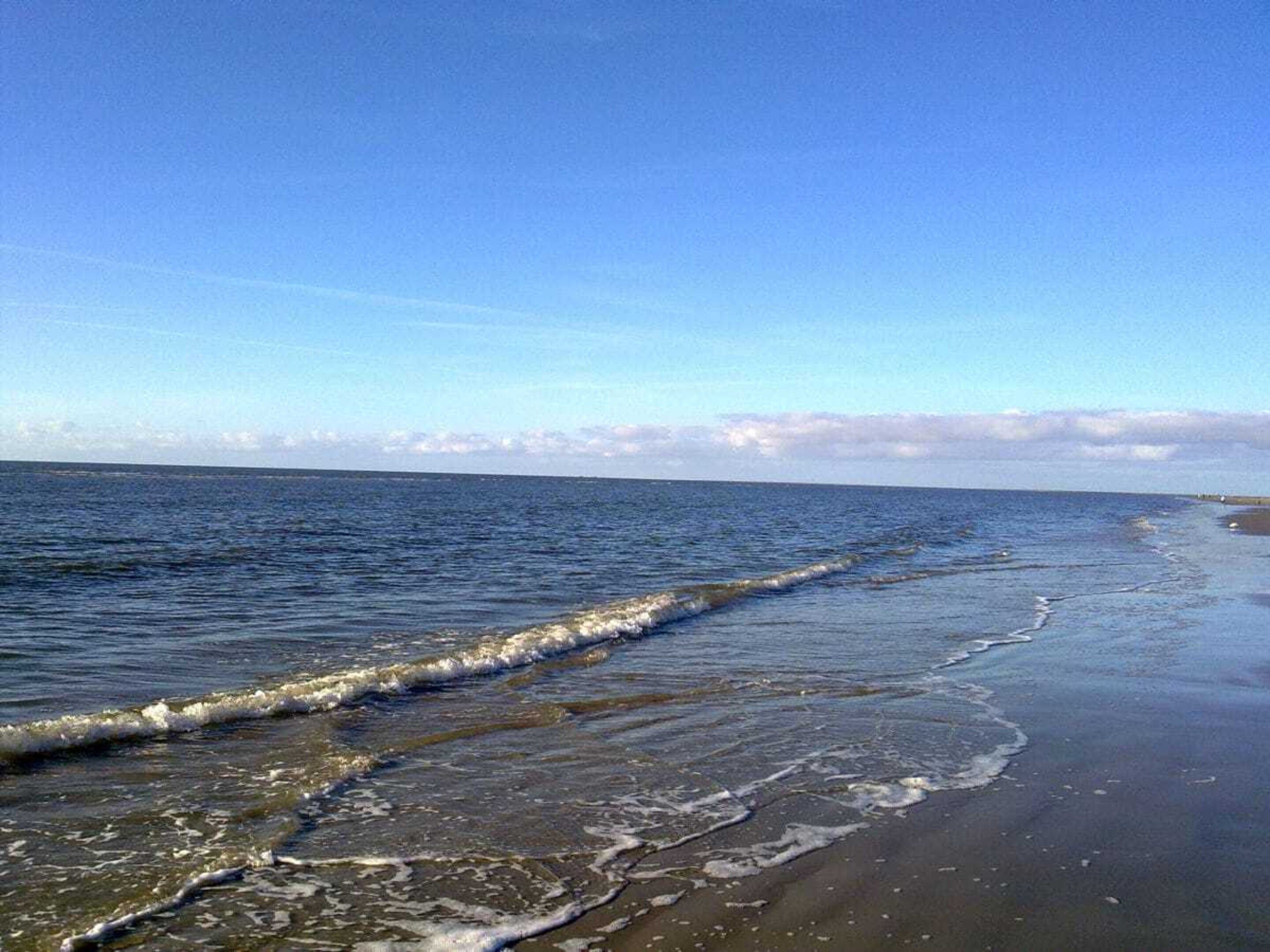 Una spiaggia con onde che lambiscono la riva, cielo sereno e una terraferma in lontananza.