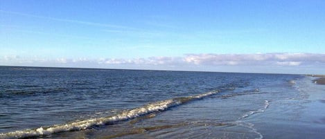 Una spiaggia con onde che lambiscono la riva, cielo sereno e una terraferma in lontananza.
