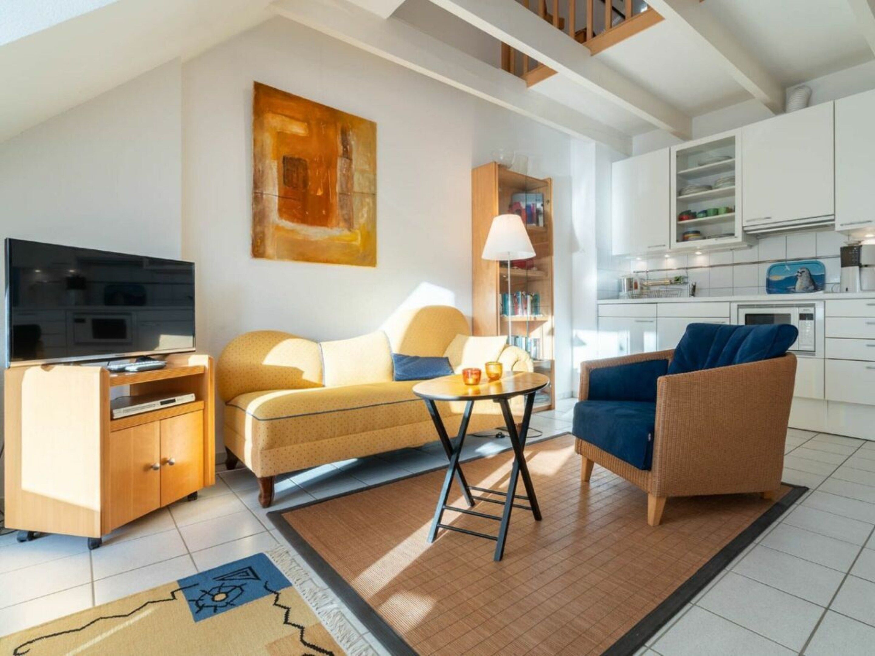 A modern living room with a sofa, a blue armchair, a coffee table, a TV, and a kitchen area in the background.