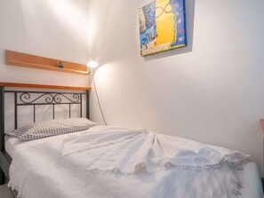 Ein Einzelbett mit Kopfstütze, einer Nachttischlampe, einem karierten Kissen und einer weißen Decke.