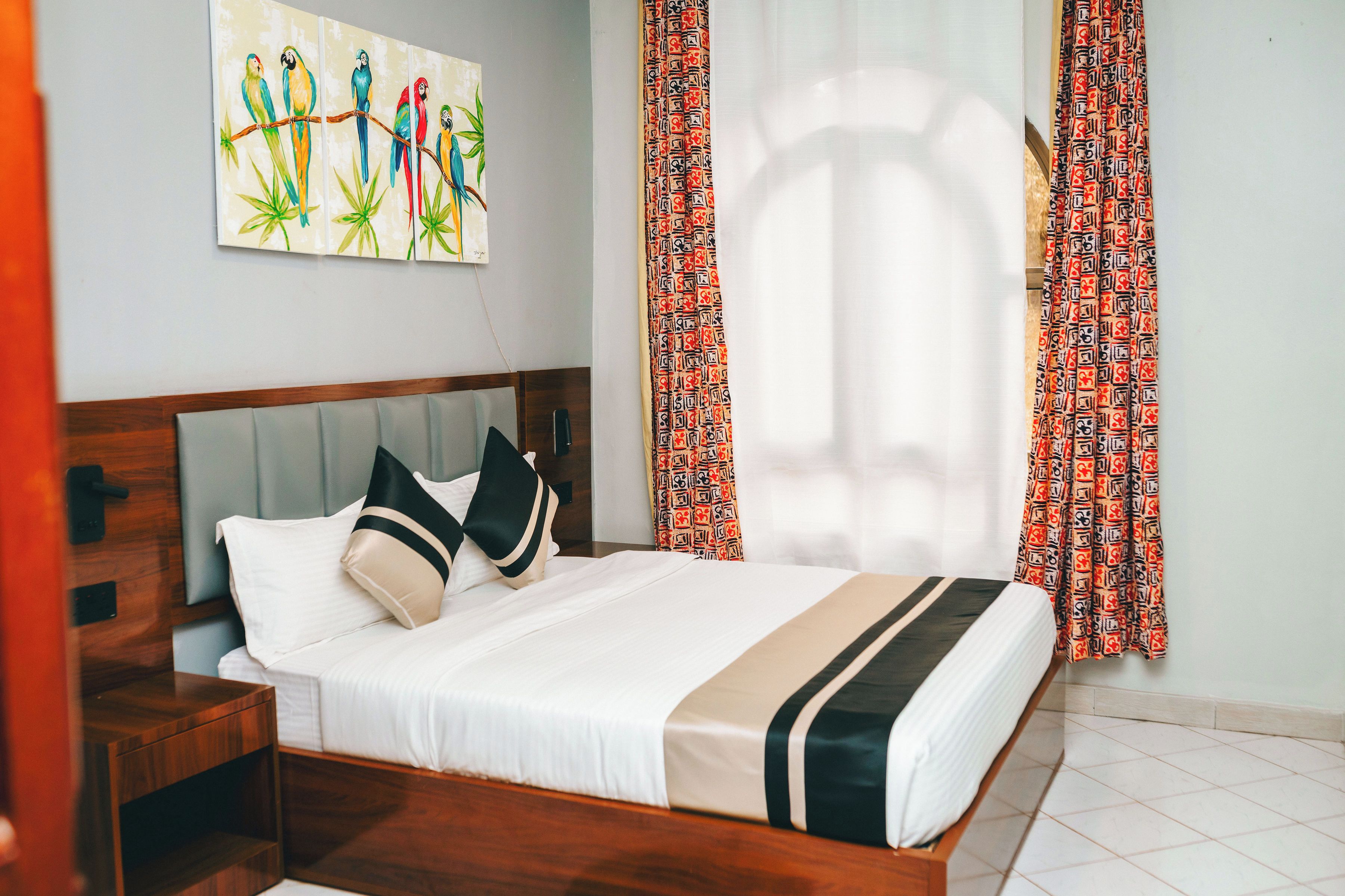 Ein Hotelzimmer mit Bett, Nachttisch, Wandbild und gemusterten Vorhängen.