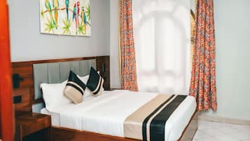 Une chambre d’hôtel avec un lit, une table de chevet, une œuvre d’art murale et des rideaux à motifs.