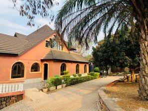 A building with a sloped roof, arched windows, and a paved pathway leading to the entrance. - Neza House (Kigali)