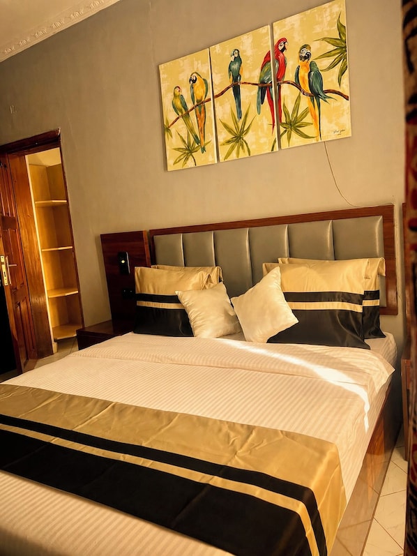 A hotel room with a large bed, a wooden headboard, and a wall-mounted painting of birds.