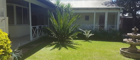Un edificio con un portico coperto, un prato curato e una fontana in pietra decorativa.