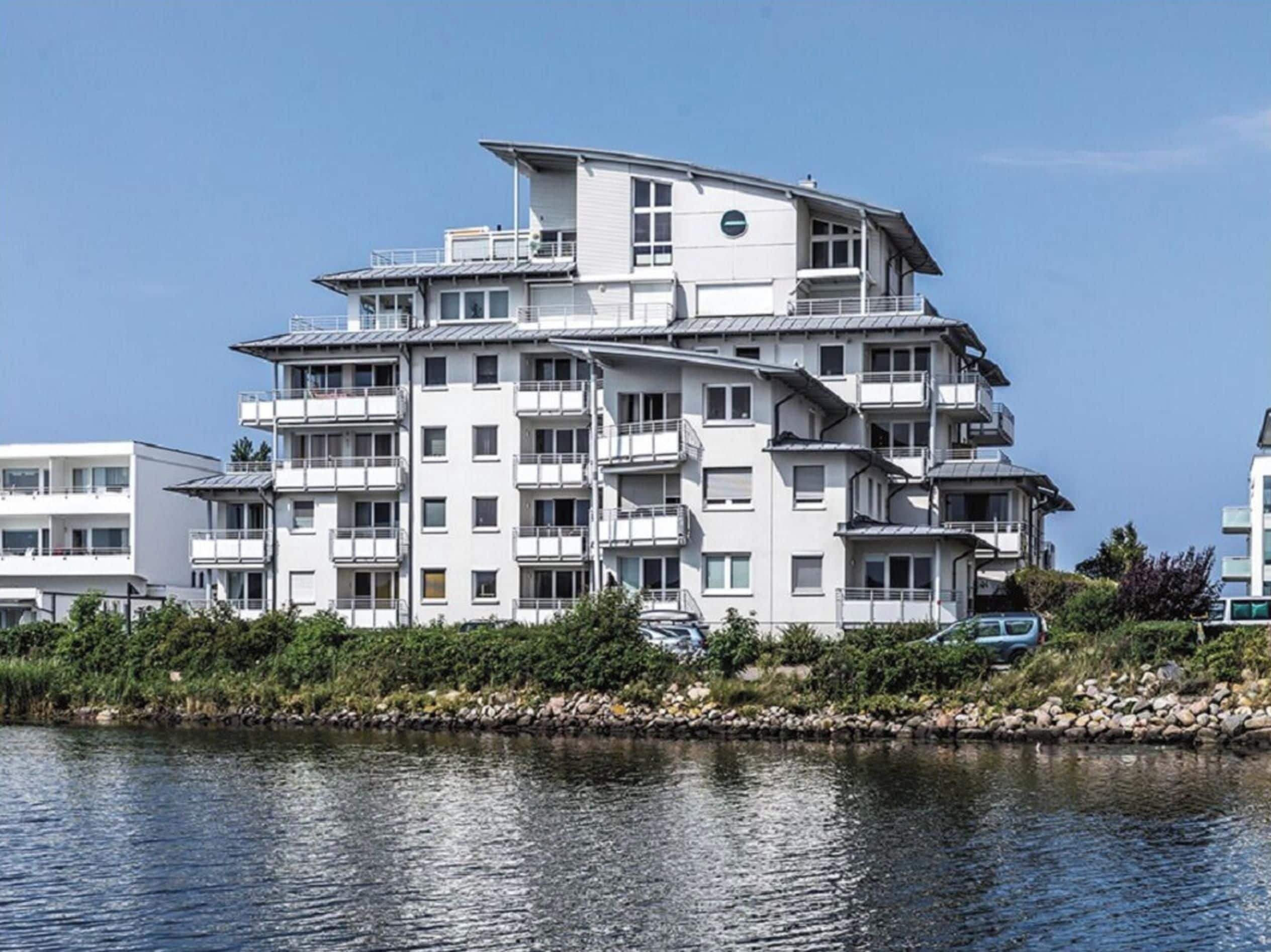 A multi-story residential building with balconies, located near a body of water.