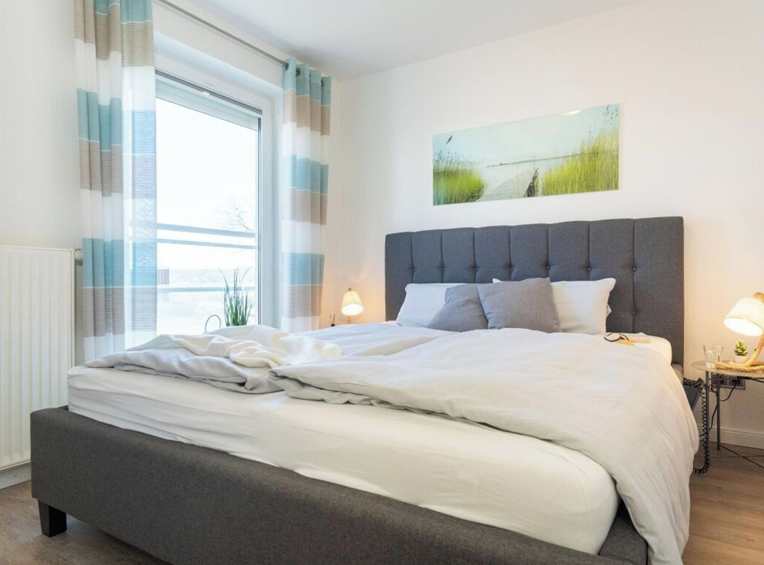 Une chambre à coucher avec un grand lit, une fenêtre avec des rideaux, une lampe de chevet et un tableau au mur.