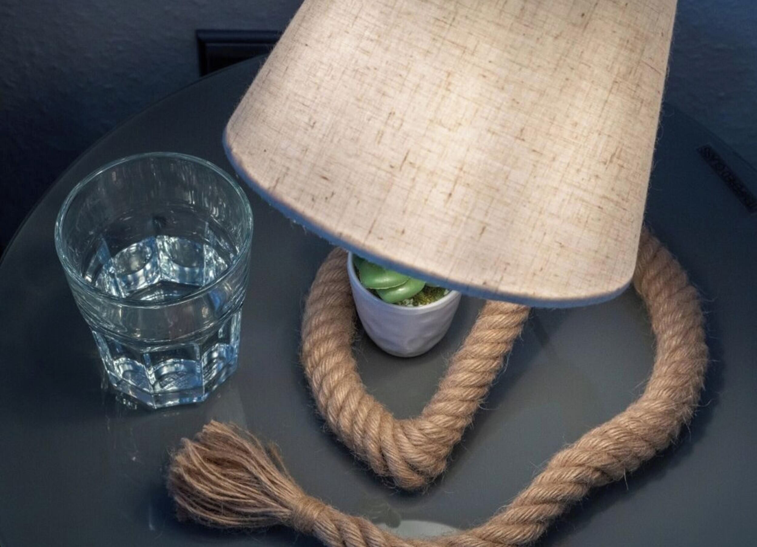 A glass of water, a lamp with a woven shade, and a rope on a table.