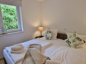 A hotel room with a bed, pillows, a bedside lamp, and a window with a view of greenery. - House by the Lighthouse Apt. 02 (St. Peter-Ording)