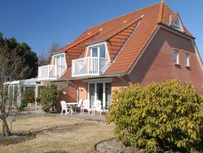 A two-story brick house with a red-tiled roof, a balcony, and a patio with outdoor furniture. - House by the Lighthouse Apt. 02 (St. Peter-Ording)