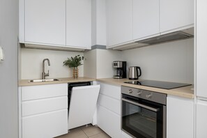 Una cocina moderna con muebles blancos, un lavamanos de acero inoxidable, una cafetera y un horno.