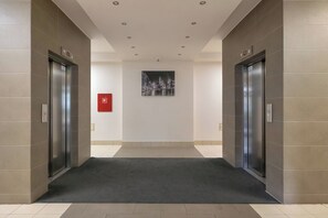 En hall med två hissar, en brandlarm och en inramad tavla på väggen.
