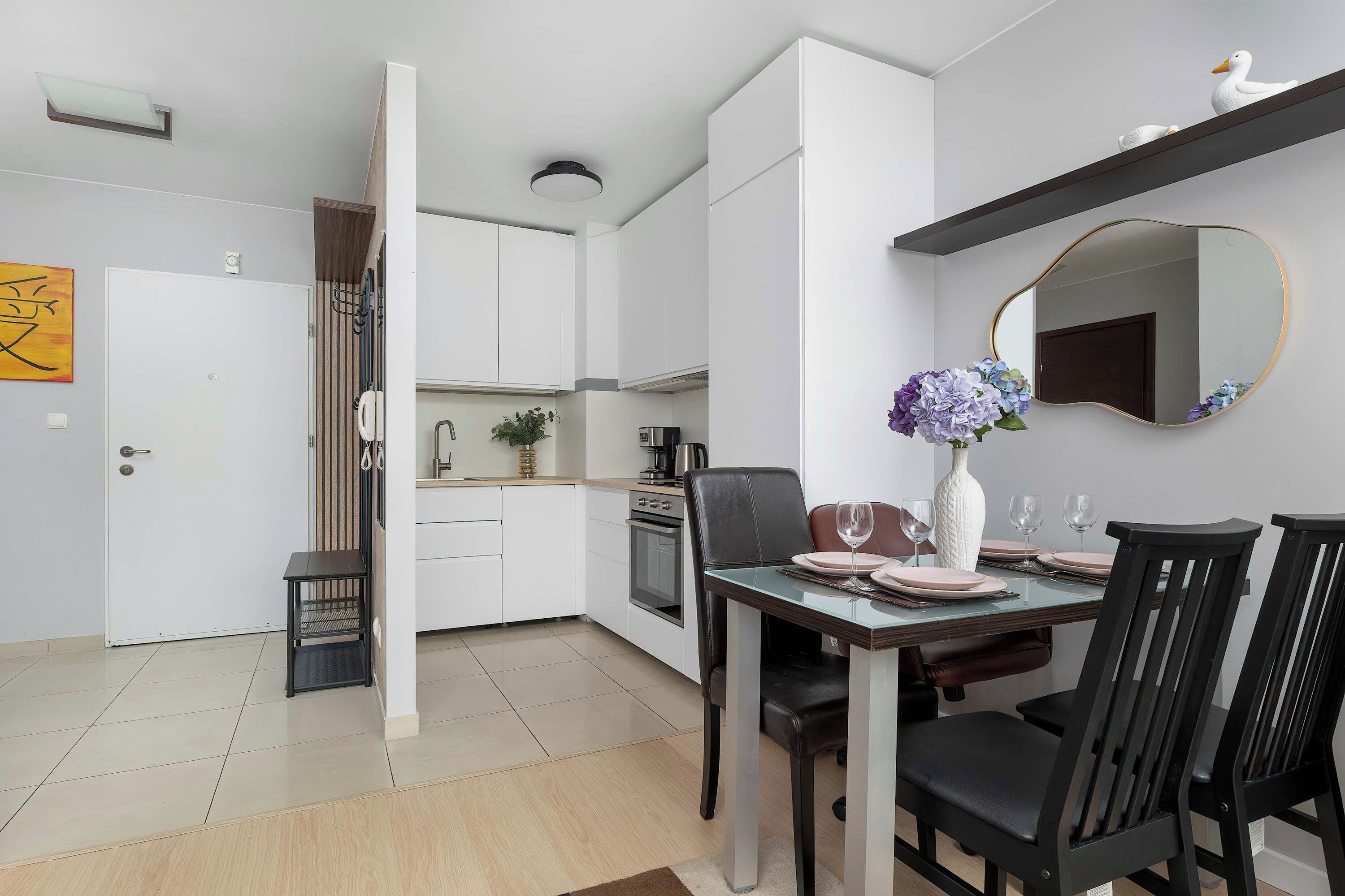 A modern kitchen with white cabinets, a dining table set for four, and a large mirror above the table.