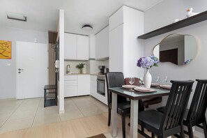 Ett modernt kök med vita skåp, ett matbord med plats för fyra personer och en stor spegel ovanför bordet.