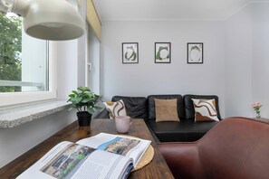Ett modernt vardagsrum med en soffa i läder, ett soffbord med en bok på och ett fönster med utsikt över grönområden.