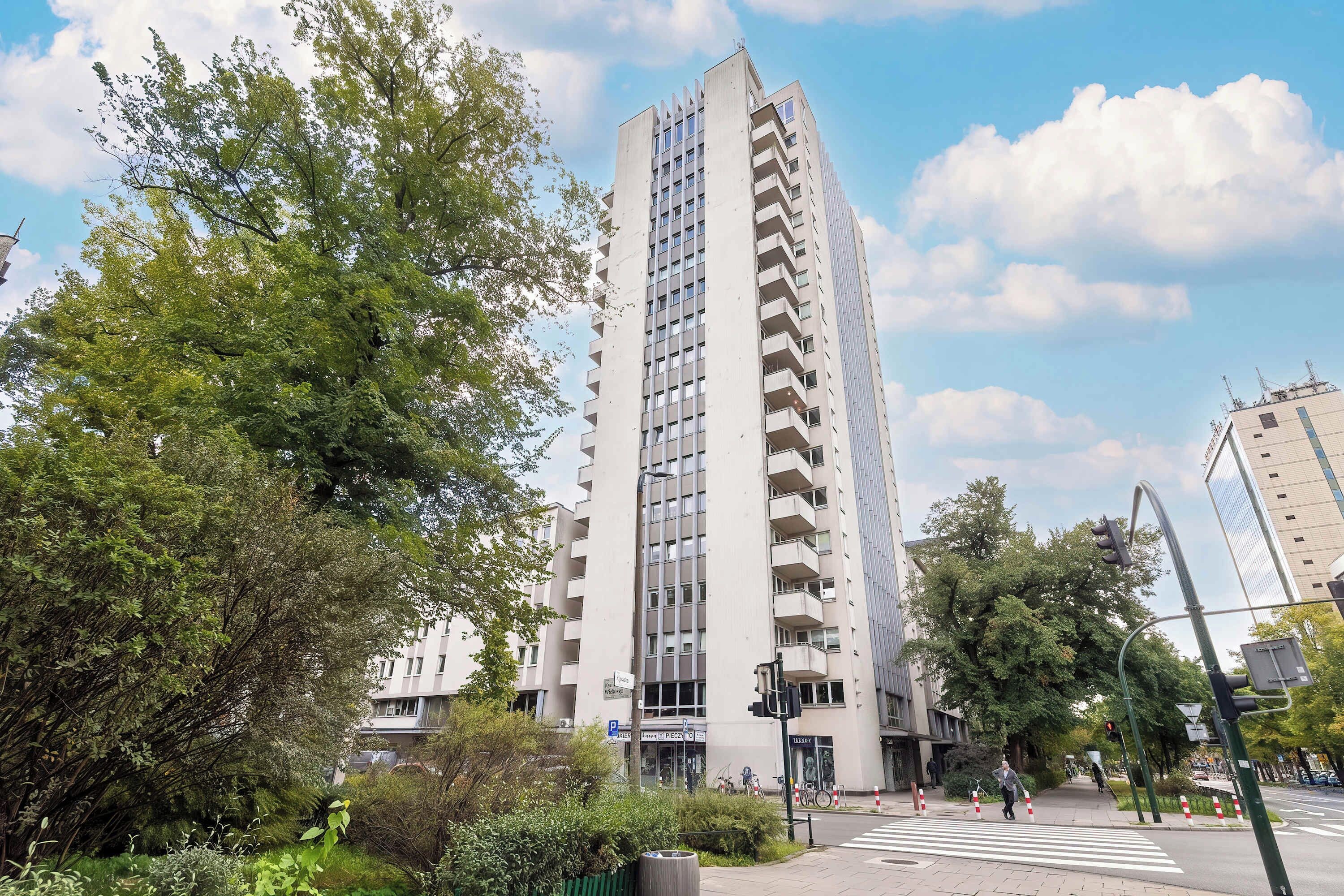 Een hoog gebouw met meerdere balkons, omgeven door groen en een heldere lucht.