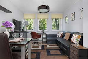 A modern living room with a dining area, a black leather sofa, a TV, and a large window with yellow blinds. - Cracow | aleja Kijowska 24 | Comfortable Apartment | Desk (Kraków)