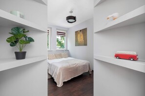 A minimalist bedroom with a bed, a potted plant, a painting, and a toy car on shelves. - Cracow | aleja Kijowska 24 | Comfortable Apartment | Desk (Kraków)