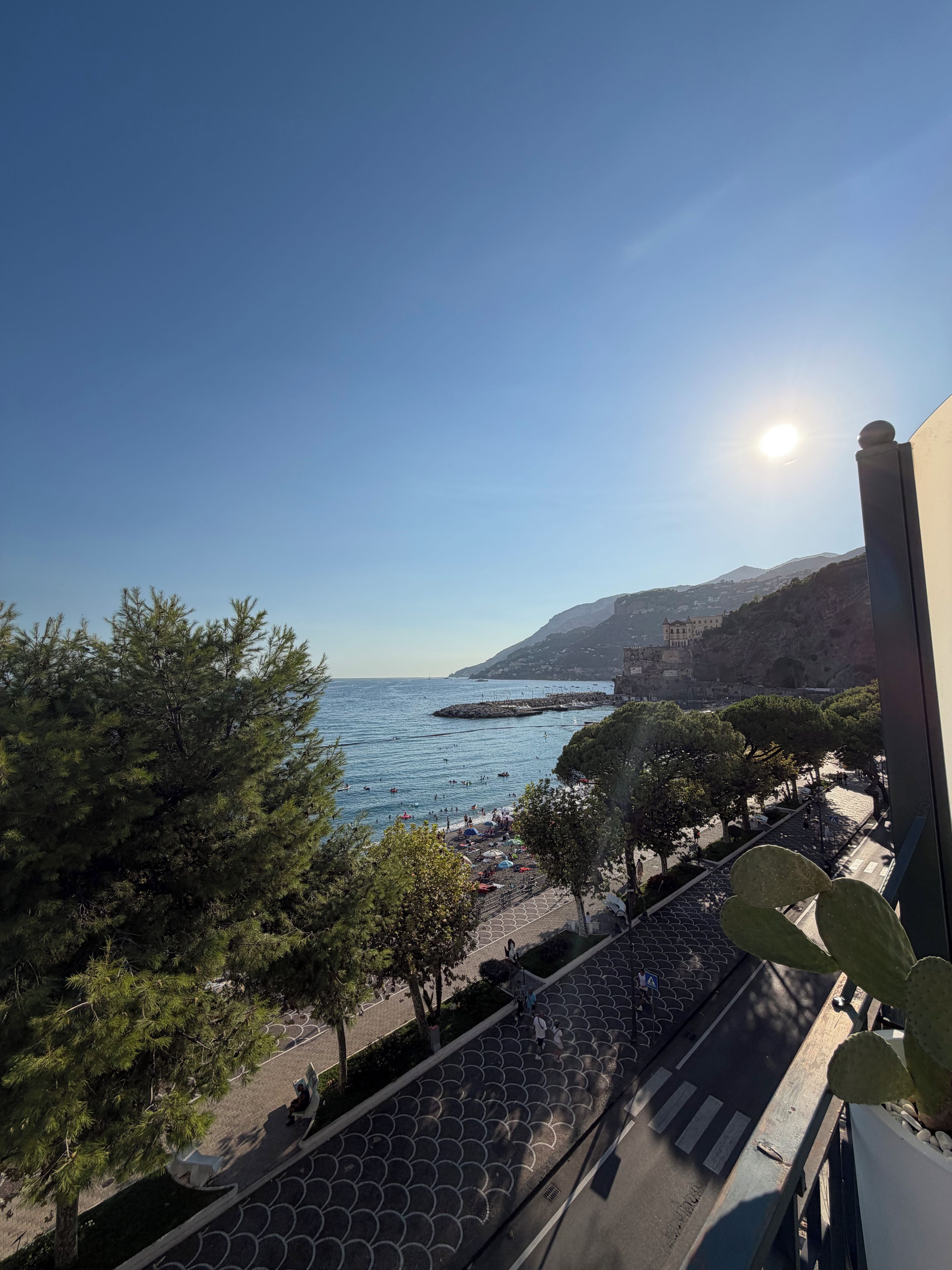 A coastal view with a clear sky, a beach with people, and a building in the background.