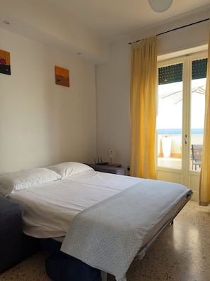 A bedroom with a bed, a desk, and a view of the sea through a door. - Rooftop Infinity Room with Ocean View (Maiori)