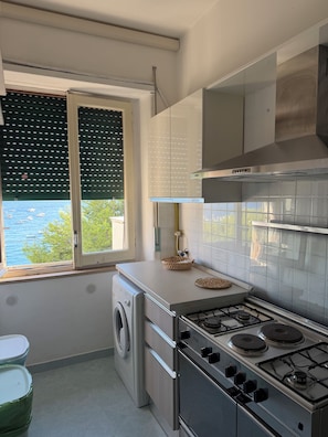 A kitchen with a washing machine, a stove, and a window with blinds. - Rooftop Infinity Room with Ocean View (Maiori)
