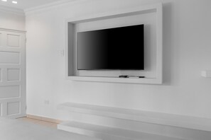 A modern, minimalist room with a large flat-screen TV mounted on a white wall. - Opal Luxury Estate | 6BR Villa, Private Pool & BBQ (Noord)