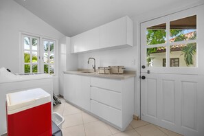 A kitchen with white cabinets, a sink, and a window with a view of greenery. - Opal Luxury Estate | 6BR Villa, Private Pool & BBQ (Noord)