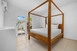 A four-poster bed with a wooden frame and white bedding in a room with white walls and tiled flooring. - Opal Luxury Estate | 6BR Villa, Private Pool & BBQ (Noord)