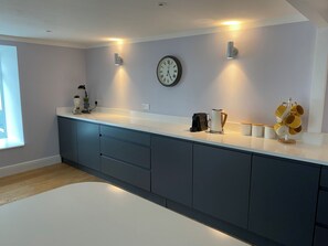 A modern kitchen with a white countertop, dark cabinets, a clock, and a coffee maker.