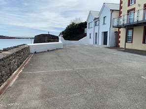 A waterfront property with a paved walkway, a stone wall, and a building with a balcony.