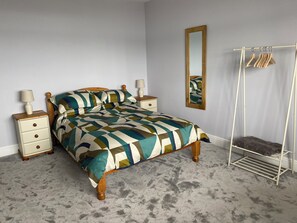A bedroom with a bed, nightstands, a mirror, and a clothing rack.
