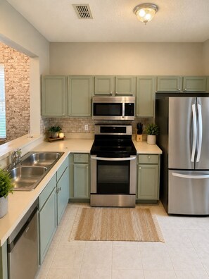 A modern kitchen with stainless steel appliances, green cabinets, and a brick accent wall. - Spacious Modern Resort Townhome Sleeps 10 with Pools, Lazy River and Near Disney (Davenport)
