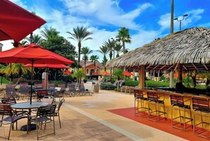 An outdoor patio area with tables and chairs, a thatched-roof structure, and palm trees. - Spacious Modern Resort Townhome Sleeps 10 with Pools, Lazy River and Near Disney (Davenport)