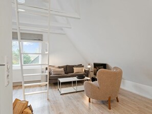 A modern living room with a loft bed, a sofa, a coffee table, and a chair. - Sonnengold Apartment Sonnengold (St. Peter-Ording)