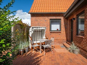 Ein Ziegelhaus mit einem Ziegeldach, eine Terrasse mit Tisch und Stühlen sowie Kübelpflanzen.