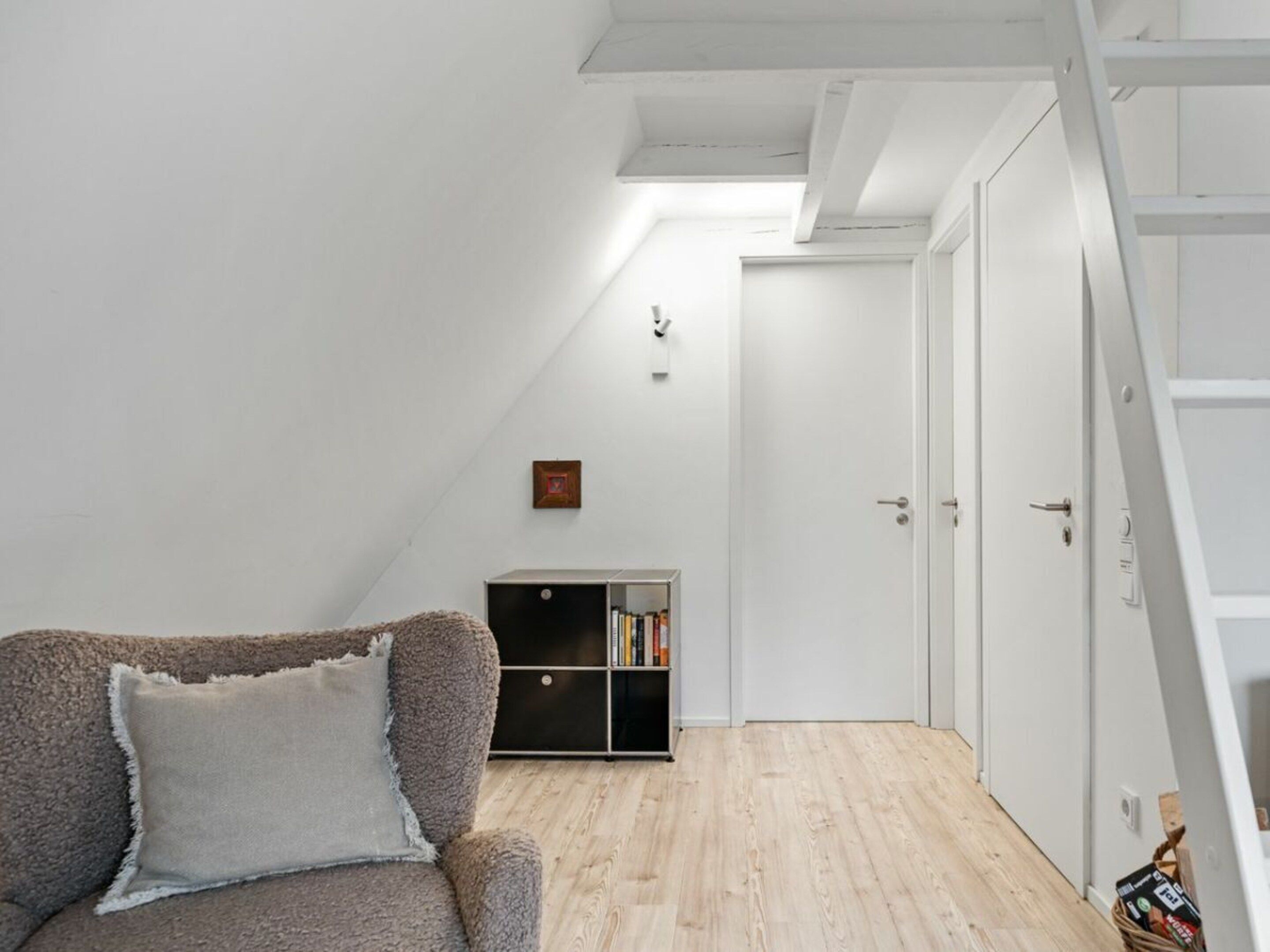 A room with a sloped ceiling, a sofa, a bookshelf, and a door.