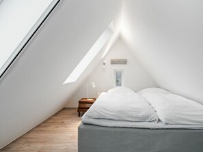 A small, well-lit attic bedroom with a sloped ceiling, a single bed, a nightstand, and a window. - Sonnengold Apartment Sonnengold (St. Peter-Ording)