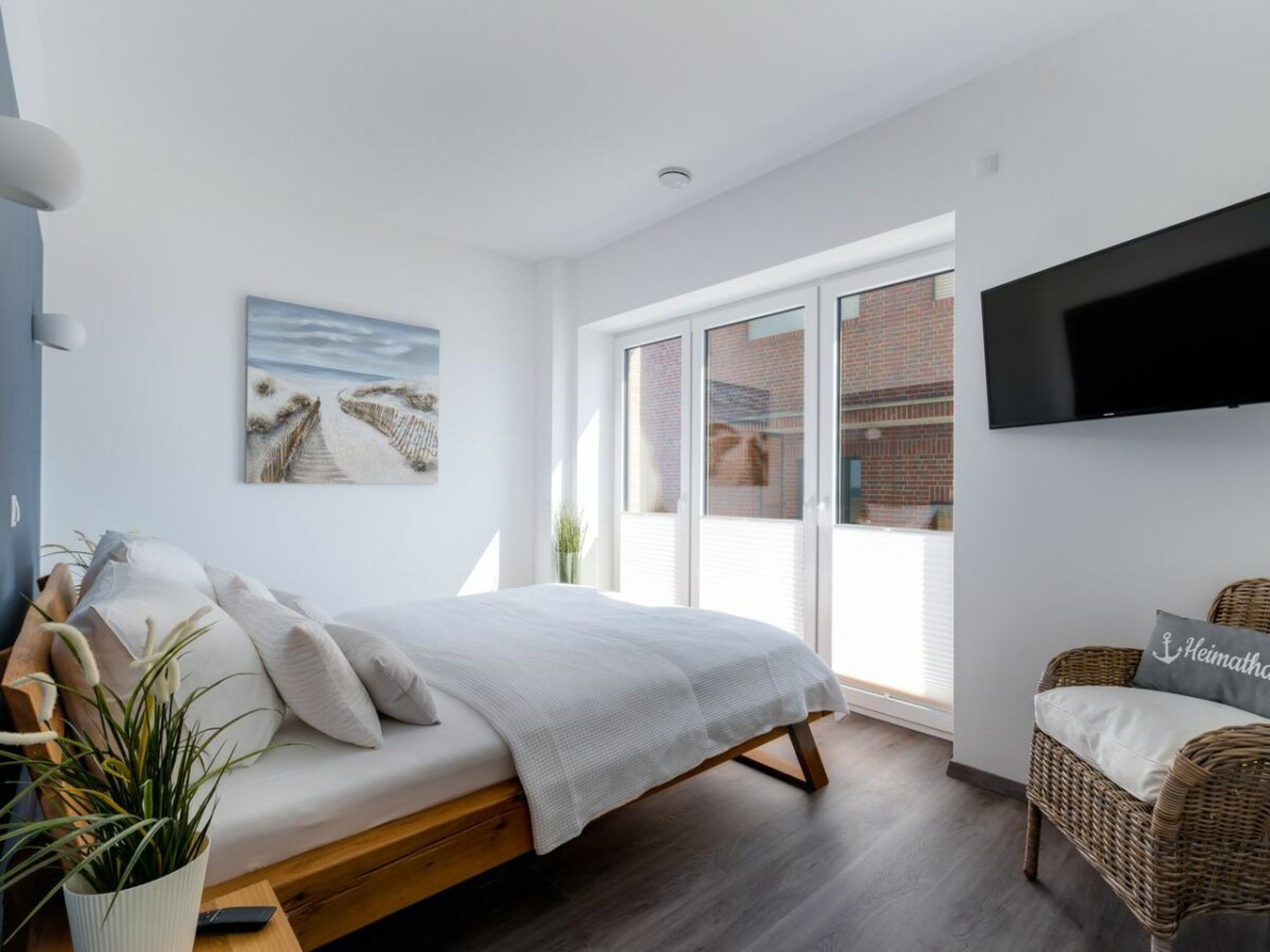 A modern bedroom with a bed, a television, a painting, and a view of the outside.