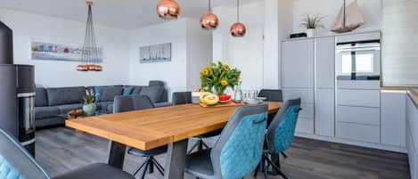 A modern kitchen with a wooden table, blue chairs, and copper pendant lights.