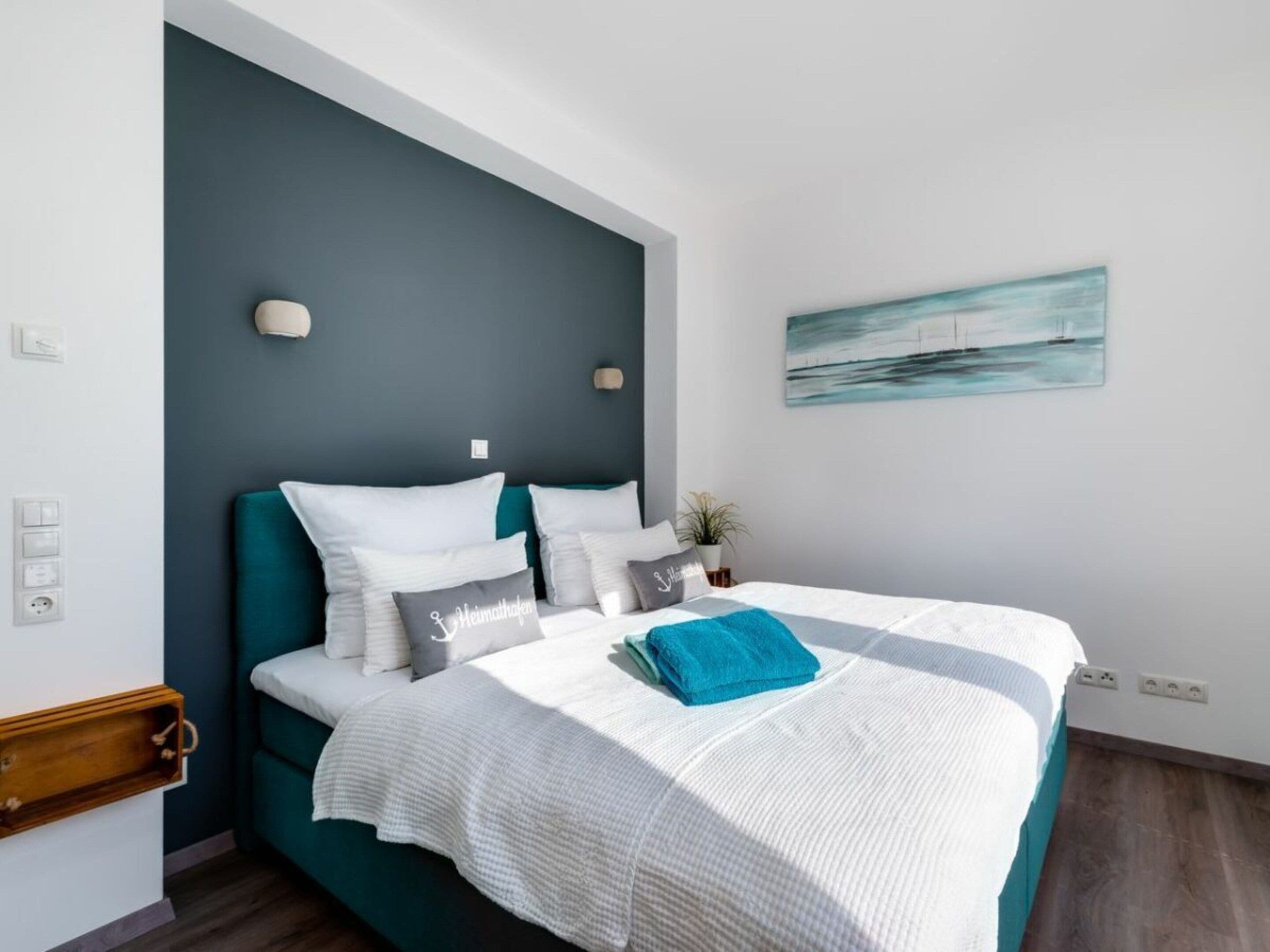 A bedroom with a bed, a nightstand, a wall-mounted light, and a painting.